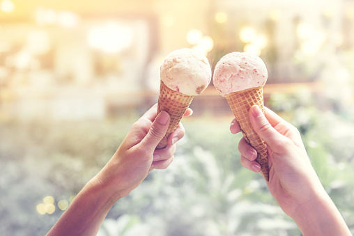 two hands hold ice cream cones in the summer sunlight